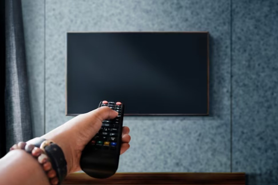 a hand holding a TV remote pointed at a television screen hanging on the wall