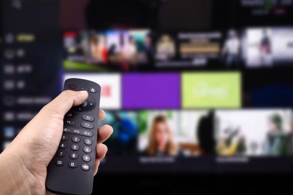 a hand holding a remote control in front of a smart TV