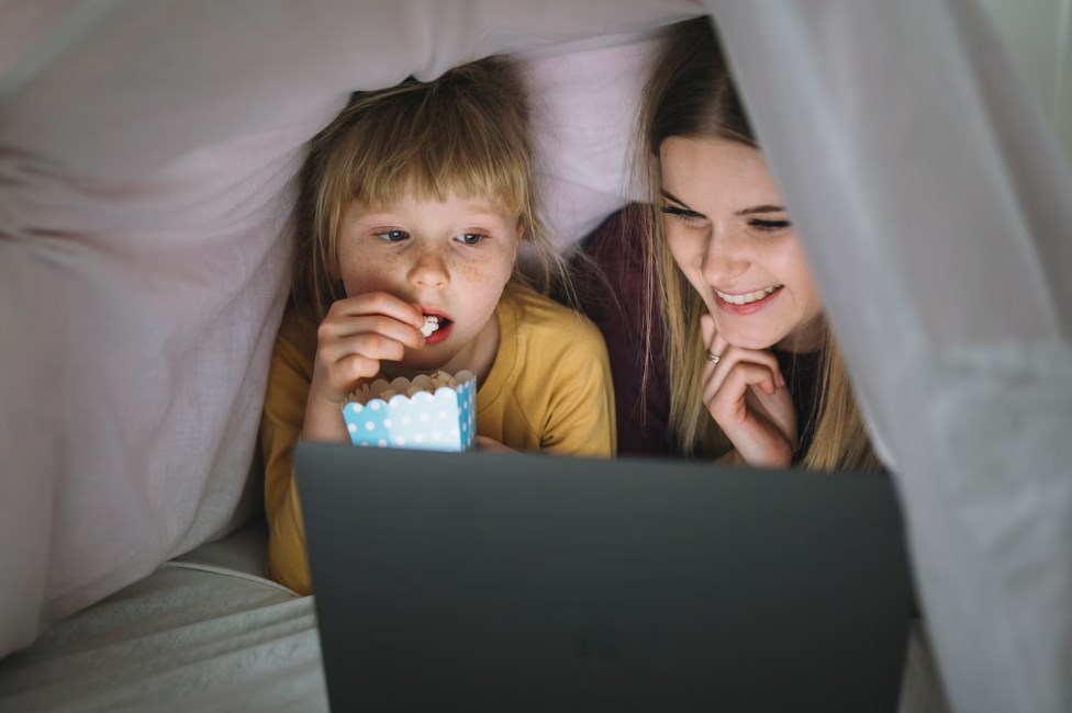 two sisters watching something on a tablet and eating popcorn