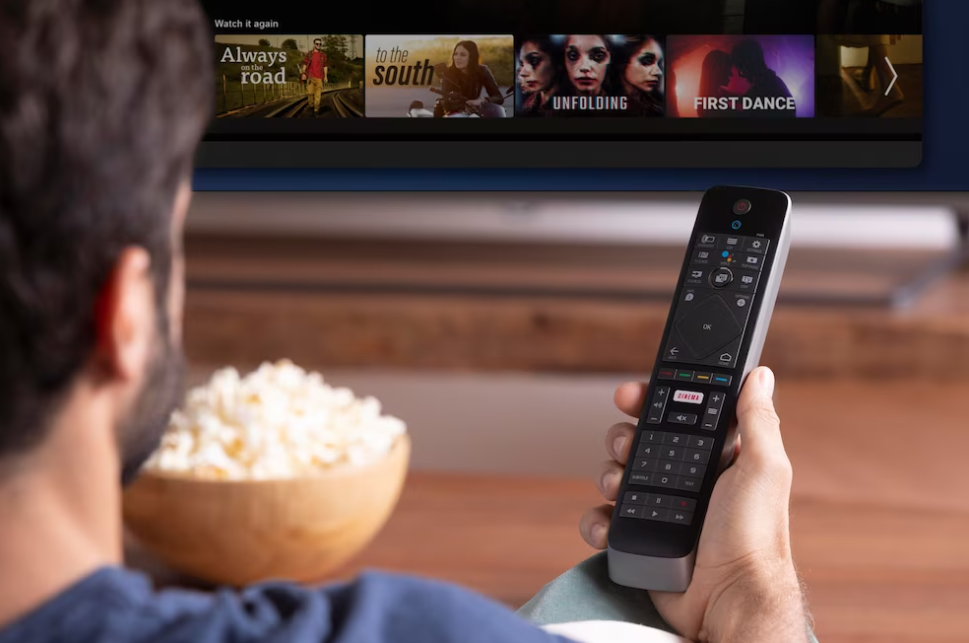 man sitting on the couch holding a tv remote control, popcorn, and watching TV