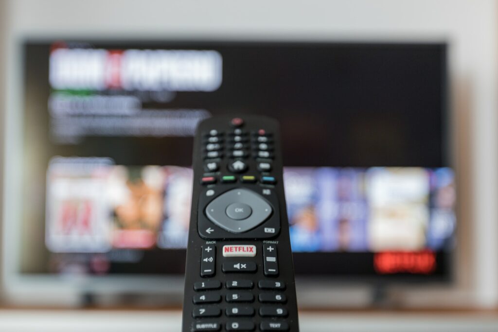 a hand holding a TV remote pointed at a television screen hanging on the wall