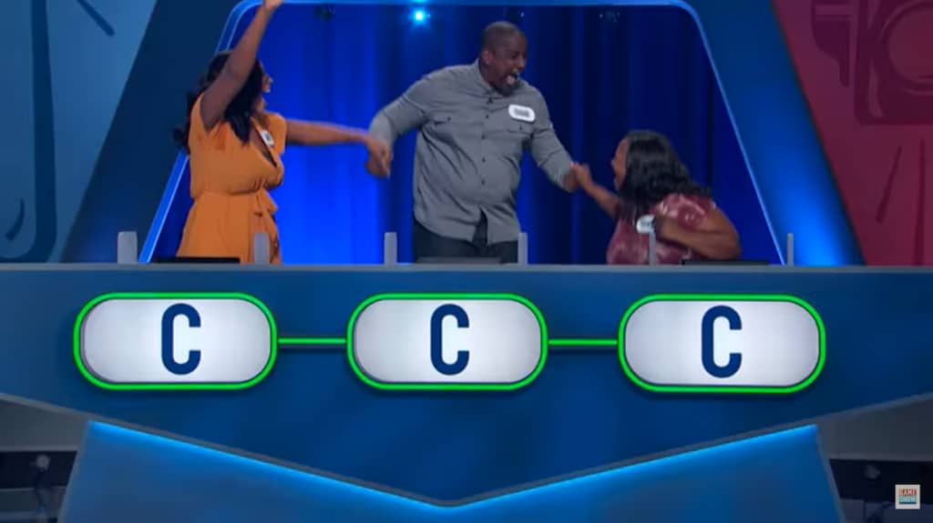 Contestants celebrate on a game show set with the letter 'C' on podiums